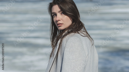 attractive young woman in coat near frozen river