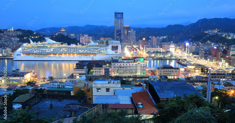Panorama of Keelung City at dusk, a busy seaport in northern Taiwan, with view of a cruise liner parking in the harbor and buildings by the quayside in blue twilight