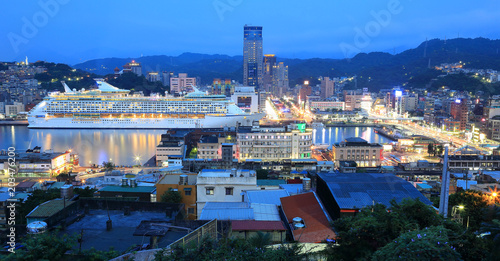 Panorama of Keelung City at dusk, a busy seaport in northern Taiwan, with view of a cruise liner parking in the harbor and buildings by the quayside in blue twilight photo