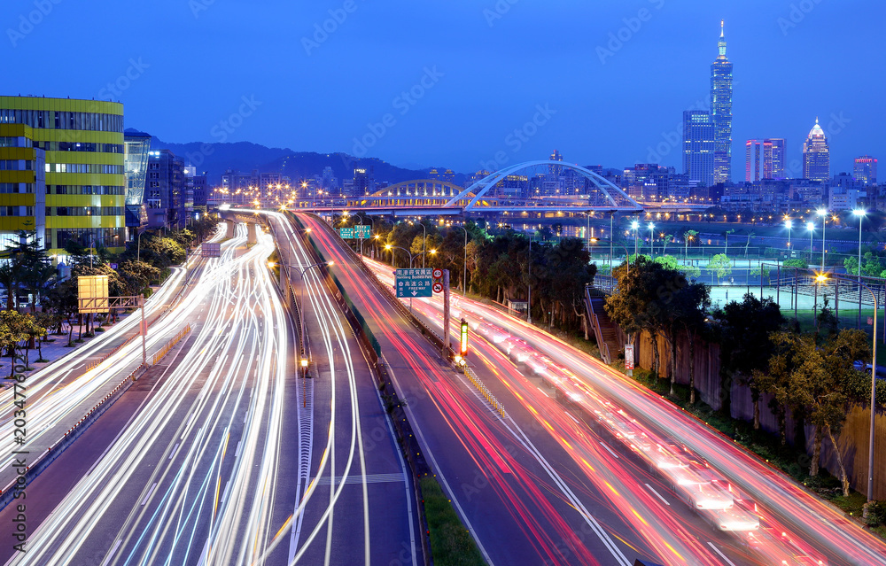 Obraz premium Night scenery of Taipei City, with Taipei 101 Tower in XinYi District, downtown area with arch bridges and car trails on Dike Avenue ~ Romantic cityscape of Taipei at dusk by riverside (long exposure)