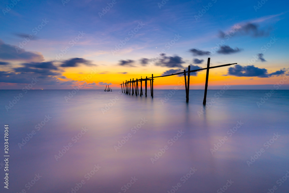 Obraz premium Silhouette of Old Abandoned and Cracked Wooden Bridge with Strong Wave in the Sea at Khao Pilai Beach in Phang Nga, Thailand. Beuatiful Sunset and Cloud in Background