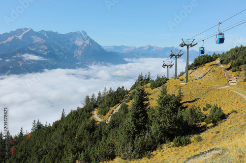 Panoramic view of magnificent Mountain Zugspitze from top of Mount Wank in Garmisch Partenkirchen, Bavaria, Germany ~ Scenic cable cars by the mountainside above sea of clouds