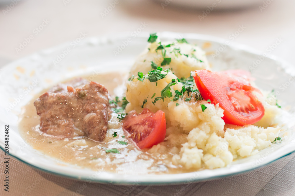 Polish traditional beef cutlets with sauce and potato and tomato slices. Beef cutlets knows in Poland as bitki wolowe.
