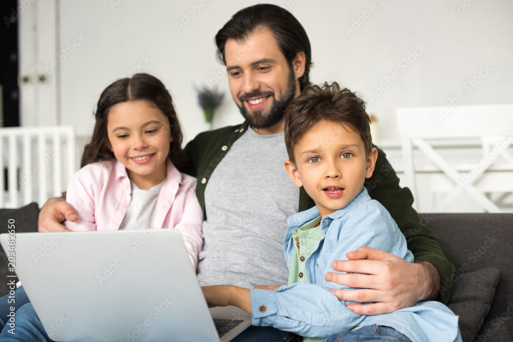 smiling father with two adorable kids using laptop together at home smiling father with two adorable kids using laptop together at home
