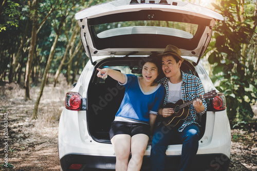 Asian couple pointing and traveling into forest by car, Musician lover. Adventure and outdoors concept. Nature and Lifestyle theme. Road trip theme.