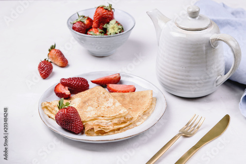 Openwork thin cheese crepes served with strawberry on grey concrete background. Homemade pancakes. Delicious breakfast