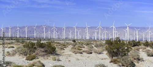 Wind turbines creating renewable energy on windfarm in desert with mountain background, a technology to move away from fossil fuels