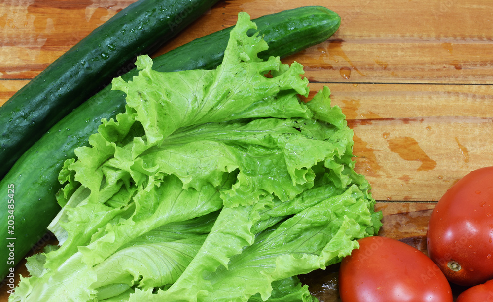 fresh juicy red tomatoes, cucumbers and lettuce on a wooden table