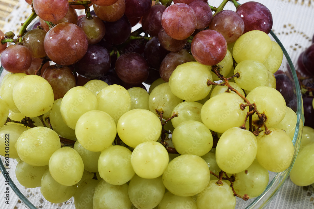 Brushes of fresh grapes of different kinds on a beautiful saucer on a wooden table Brushes of fresh grapes of different kinds on a beautiful saucer on a wooden table