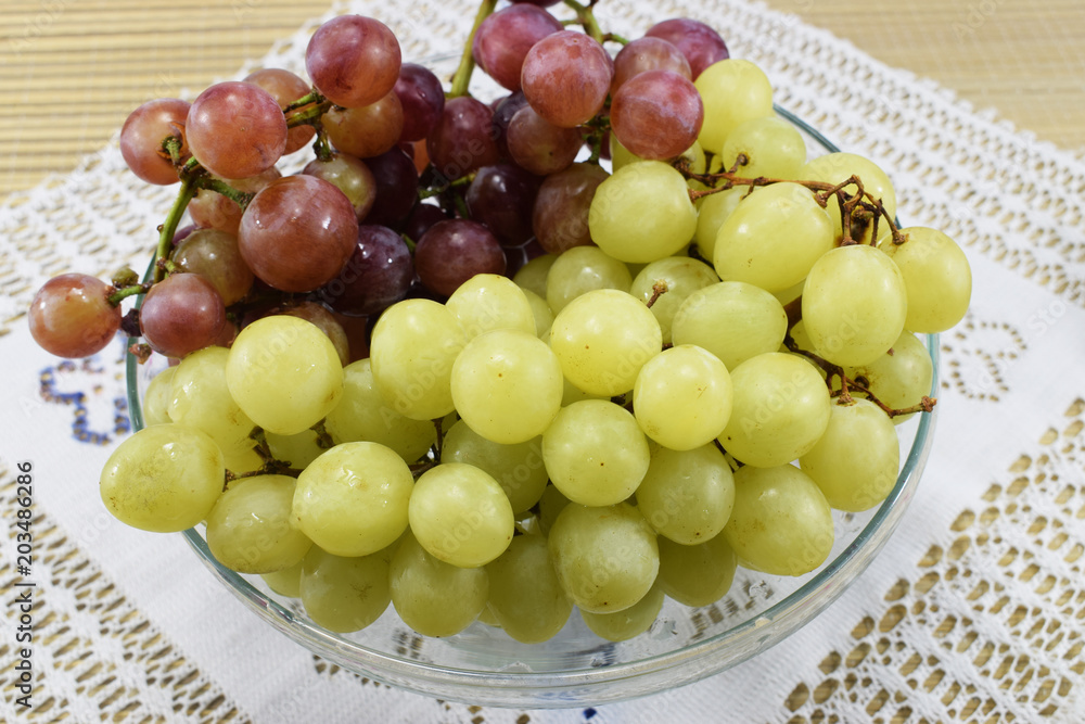 Brushes of fresh grapes of different kinds on a beautiful saucer on a wooden table