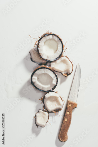 top view of pieces of natural healthy coconut and knife on white