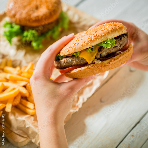 Hands hold american burger and french fries, sauce on wooden plate