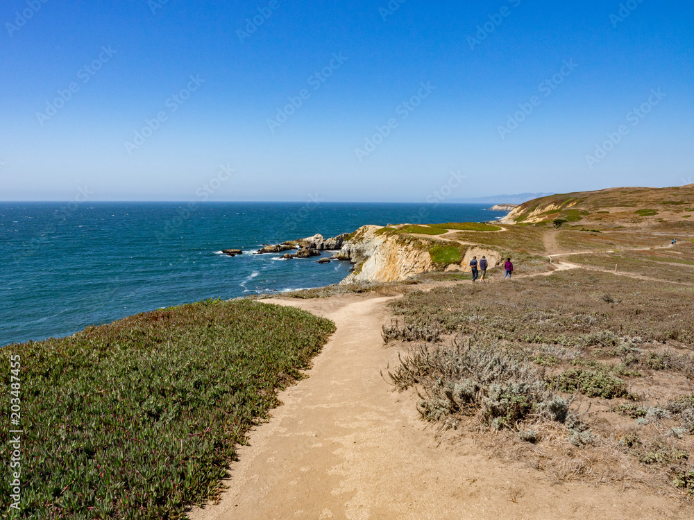 Three hikers on trail above rocky cliffs and ocean at Bodega Head Trail, Bodega Bay, California, United States on sunny summer day Three hikers on trail above rocky cliffs and ocean at Bodega Head Trail, Bodega Bay, California, United States on sunny summer day