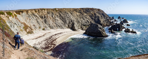 Three hikers on trail above rocky cliffs and ocean at Bodega Head Trail, Bodega Bay, California, United States on sunny summer day