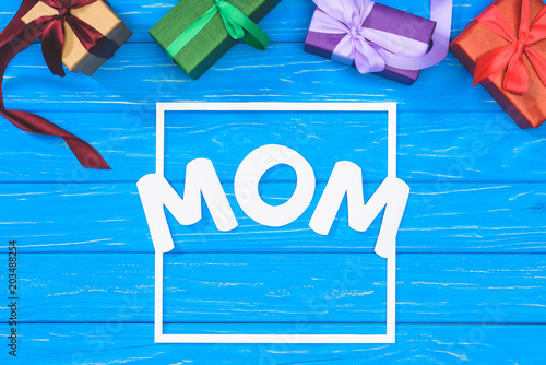 top view of gift boxes and word mom in frame on blue table, mothers day concept