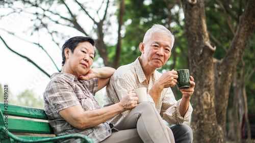 Asian senior couple relax drinking coffee in summer park, green nature © glowonconcept