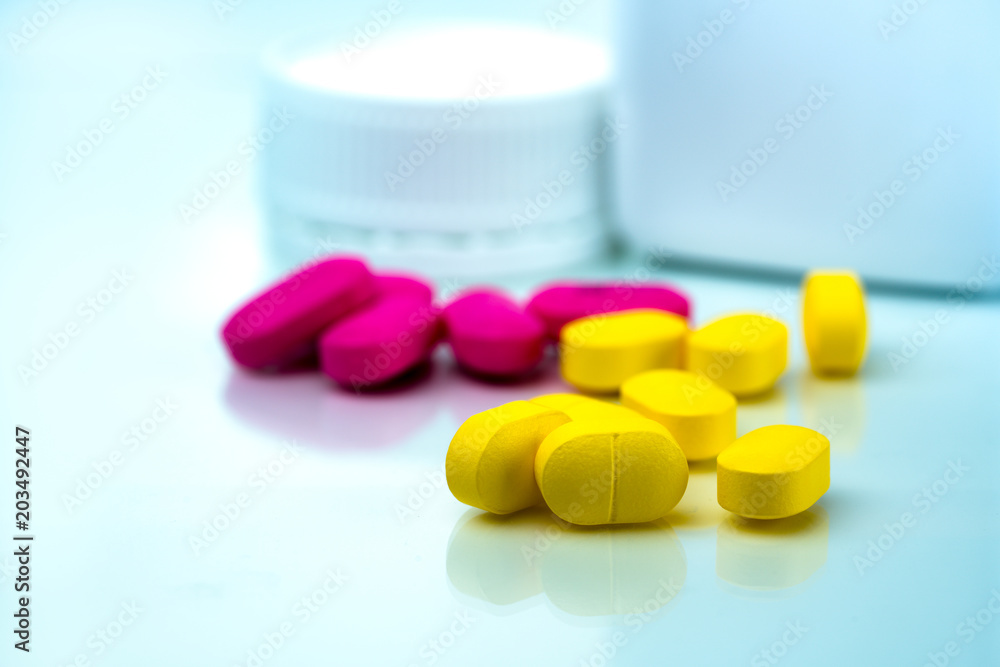 Pile of yellow and pink tablets pills on blurred background of plastic pills bottle with copy space. Ibuprofen for relief pain. Pharmaceutical industry and drugstore concept. Painkiller tablet pills Pile of yellow and pink tablets pills on blurred background of plastic pills bottle with copy space. Ibuprofen for relief pain. Pharmaceutical industry and drugstore concept. Painkiller tablet pills