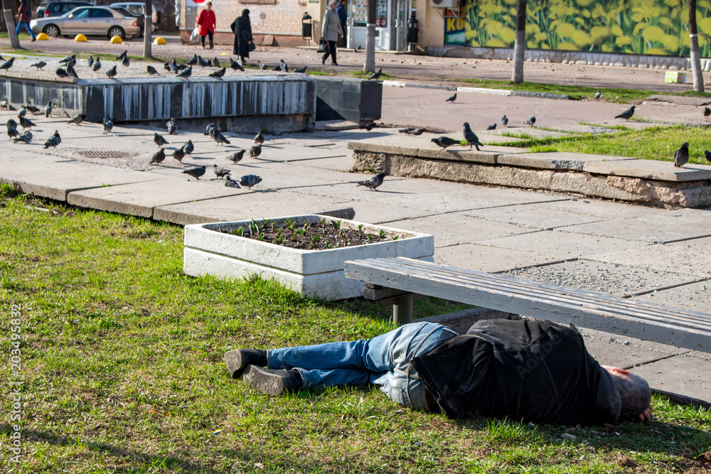 A drunk man asleep on the grass in the city