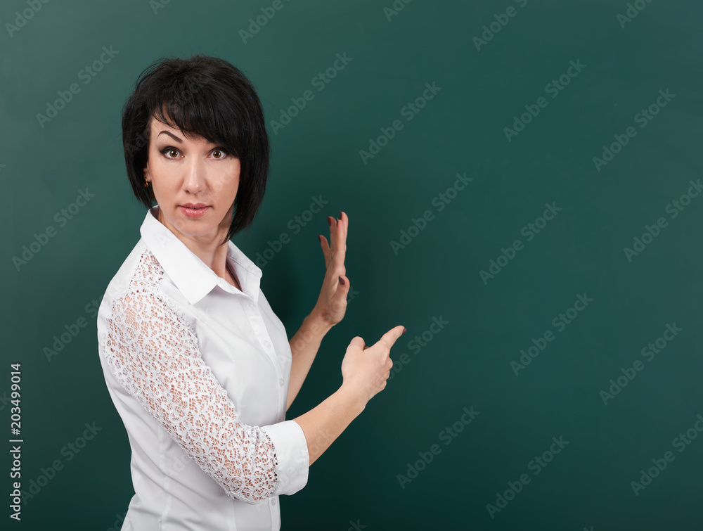 woman teacher shows on a blackboard anything, blank space for text and graphics, green background, Studio shot