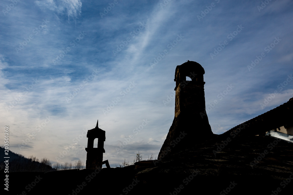 Silhouettes of two retro style chimneys and few leafless trees in Serbia with cloudy blue sky at dusk