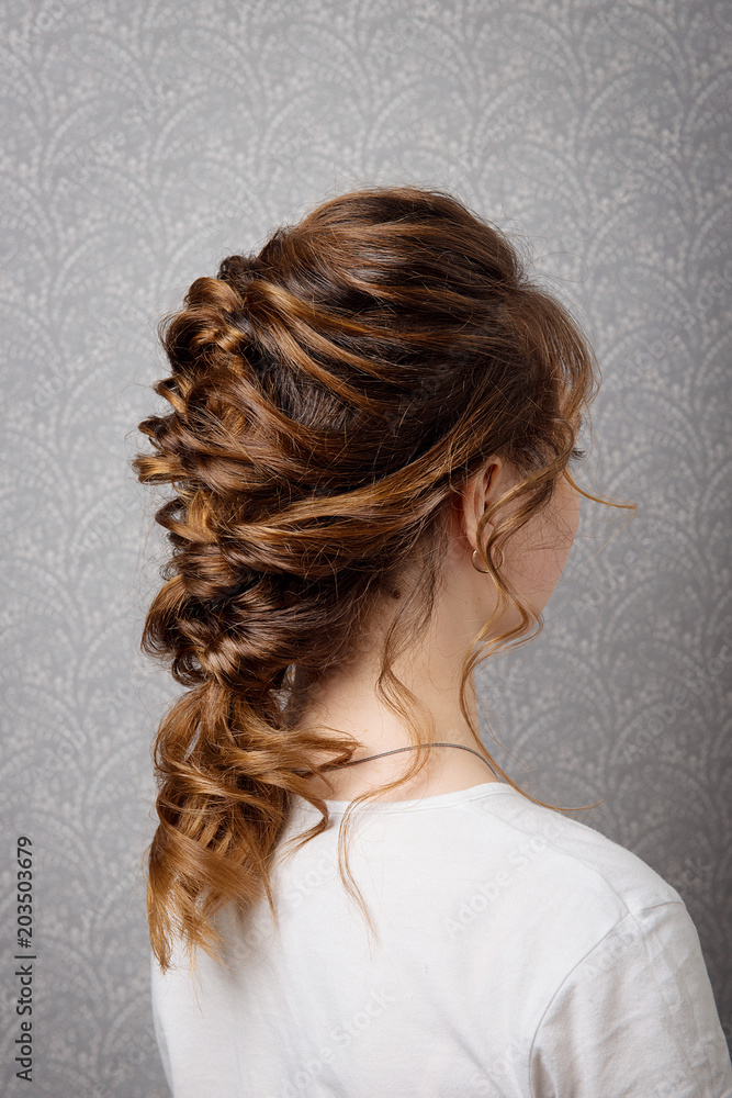 Hairstyle Greek braid on the head of a brown-haired woman back view close-up on a gray background. Hairstyle Greek braid on the head of a brown-haired woman back view close-up on a gray background.