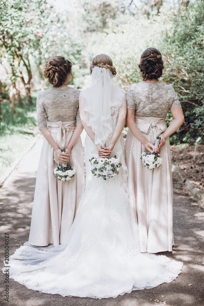 Beautiful bride with bridesmaids holding bouquets for a walk in a park after wedding ceremony, bride with friends photo Beautiful bride with bridesmaids holding bouquets for a walk in a park after wedding ceremony, bride with friends photo