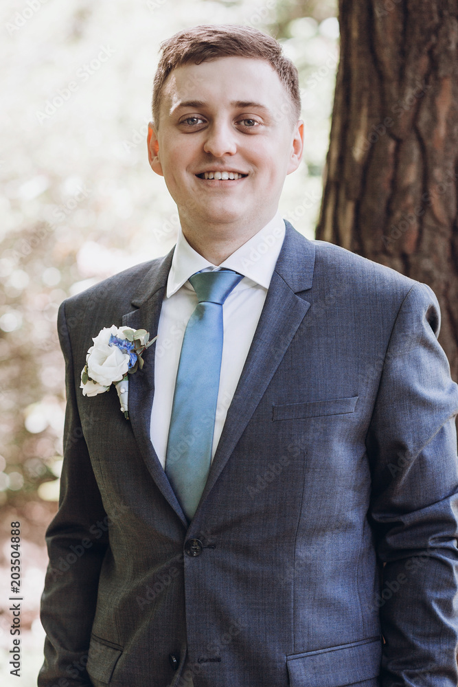 gorgeous groom in suit posing and smiling in sunny garden gorgeous groom in suit posing and smiling in sunny garden