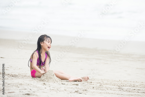 Happy child playing with sand at the beach in summer