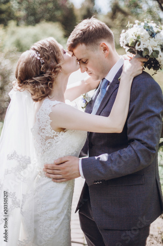beautiful gorgeous bride and groom kissing in sunny spring park and enjoying day. happy wedding couple relaxing in green garden. happy marriage moments. elopement concept