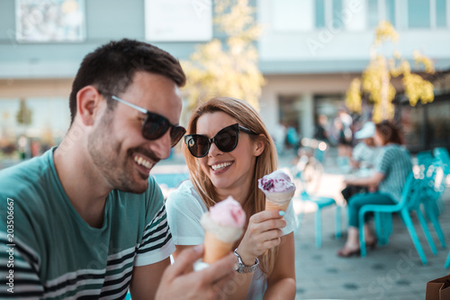 Photography A beautiful young couple with sunglasses are sitting outdoors and having ice-cre