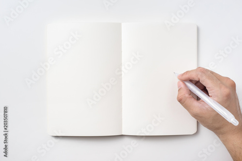 Fototapeta Naklejka Na Ścianę i Meble -  Design concept - Top view of notebook blank page and man's hand holding ballpoint pen isolated on white background for mockup