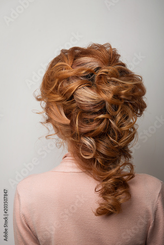 Hairstyle Greek braid on the head of a red hair woman back view close-up on a gray background.