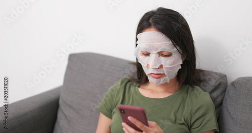 Wallpaper Mural Woman applying facial skincare mask and use of mobile phone at home Torontodigital.ca