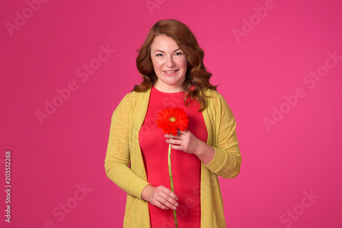 Beautiful adult woman with flowers on a pink background.