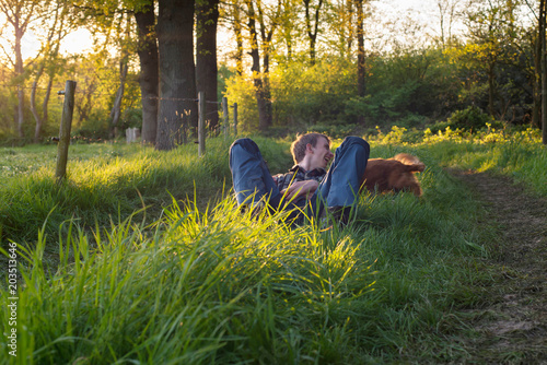 Happy teenage man having fun with dog in countryside during spring.