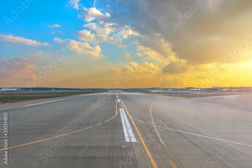 Runway at the airport in the sunset sun light sky blue gradient yellow color cumulus clouds.