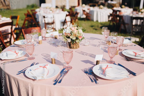 banquet wedding tables are in the backyard  plates  glasses  candles and flower and green arrangements are on the table