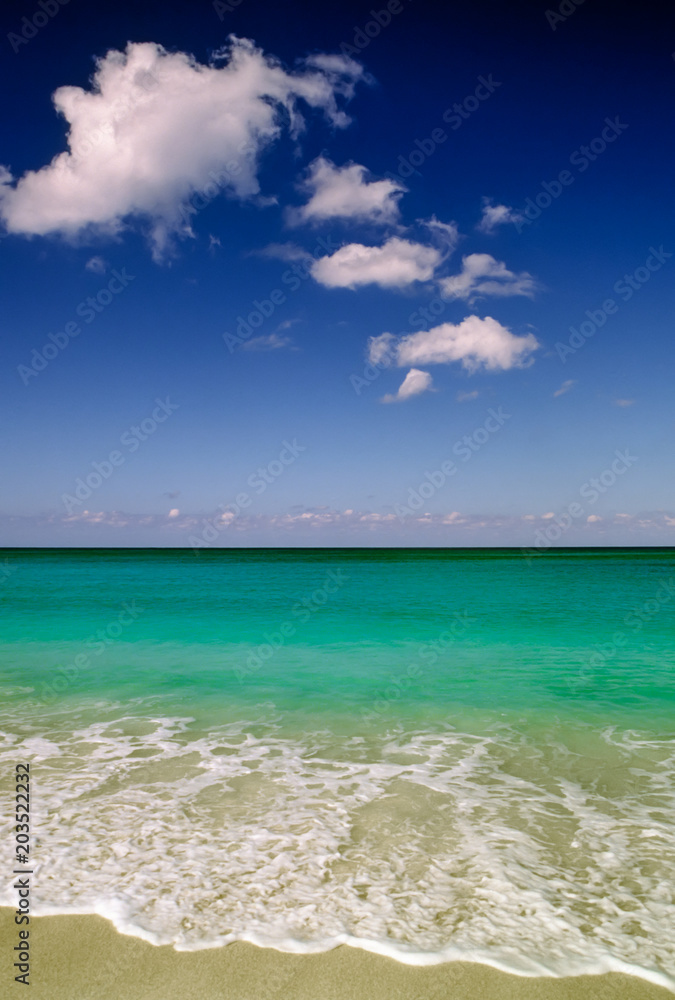 Tropical sandy beach and waves with fluffy clouds against a clear blue sky