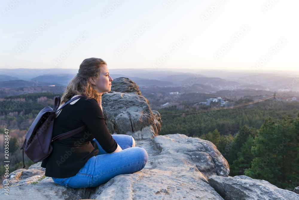 pensive girl with backpack sitting on a rock hell mountain valley at sunset
