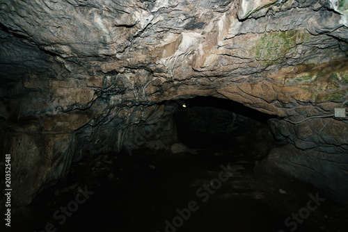 Beautiful cave. View from inside dark dungeon. Textured walls of cave. Background image of underground tunnel. Dampness inside cave. Lighting inside cave for excursions.