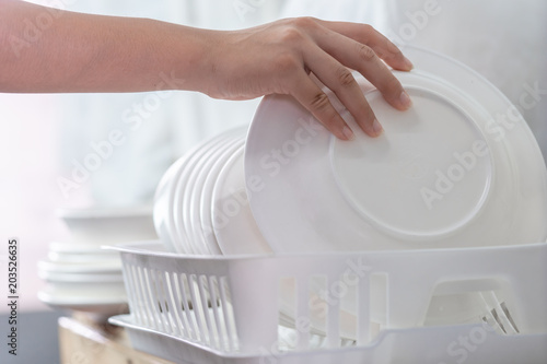 Hand of woman putting just washed clean plate in the dish rack