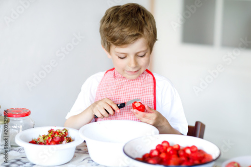 Little blond kid boy helping and making strawberry jam in summer