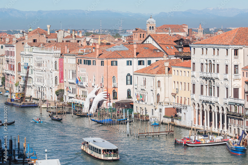 View of the Grand Canal with sailing ships, houses with red roofs and mountains in the distance, a bright sunny day in Venice, Italy.