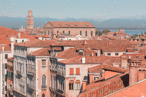 View of houses with red roofs and mountains in the distance, a bright sunny day in Venice, Italy.
