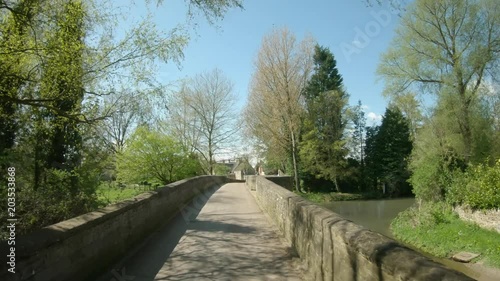 Driving over the narrow mediaeval bridge built over the river Ise in 1250 in the village of Geddington in Northamptonshire in England. Vehicle POV. photo