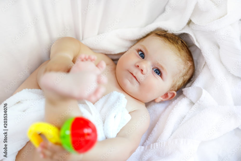 Cute little baby playing with toy rattle and own feet after taking bath. Adorable beautiful girl wrapped in white towels Cute little baby playing with toy rattle and own feet after taking bath. Adorable beautiful girl wrapped in white towels