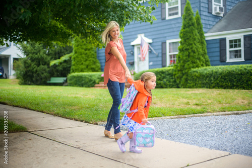 Mid adult woman walking with eager daughter on suburban sidewalk photo