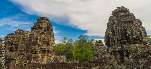 View of several ancient towers with smiling face sculptures of the famous Bayon temple (orig.: Jayagiri) in Cambodia.