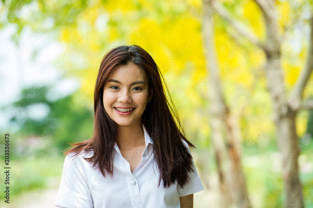 portrait of the happy beautiful Thai student with university uniform standing and smiling on the yellow tree background portrait of the happy beautiful Thai student with university uniform standing and smiling on the yellow tree background