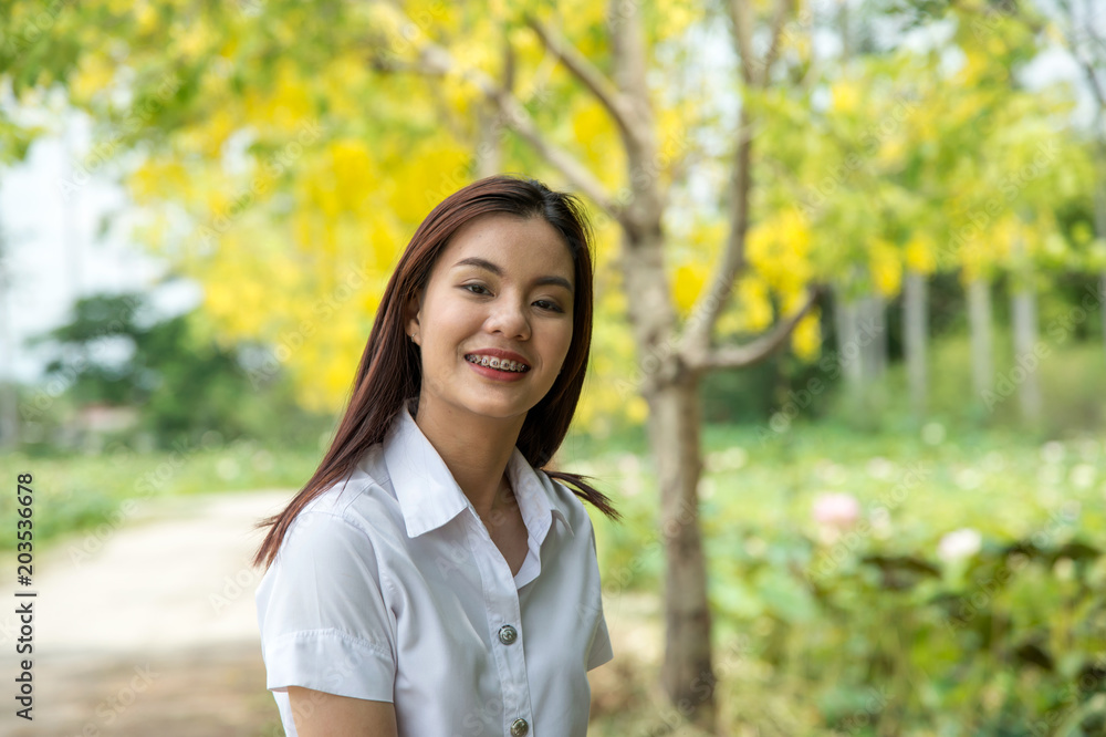 portrait of the happy beautiful Thai student with university uniform standing and smiling on the yellow tree background portrait of the happy beautiful Thai student with university uniform standing and smiling on the yellow tree background